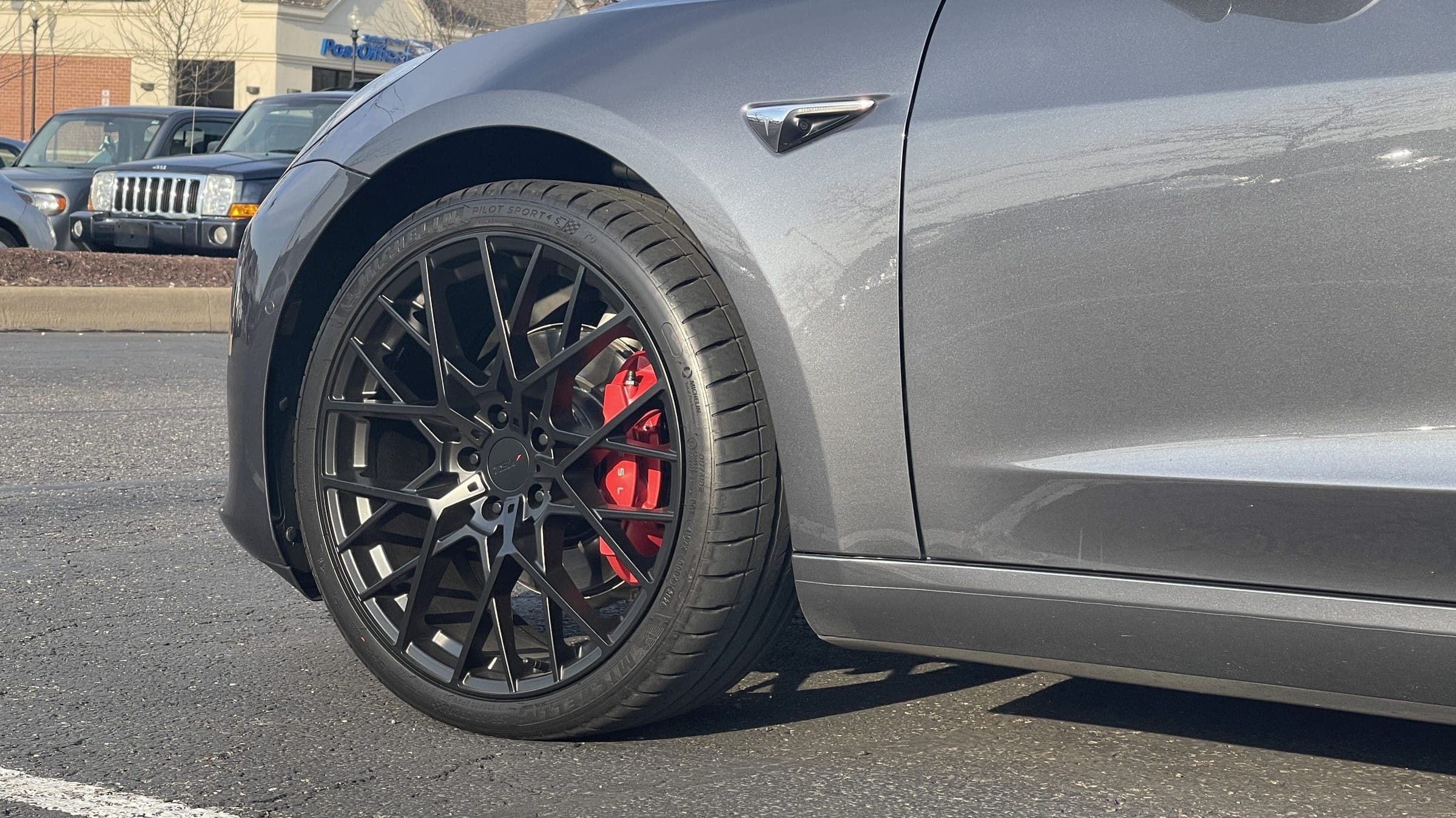 Close-up of a grey Model 3's black multi-spoke wheel and red caliper.